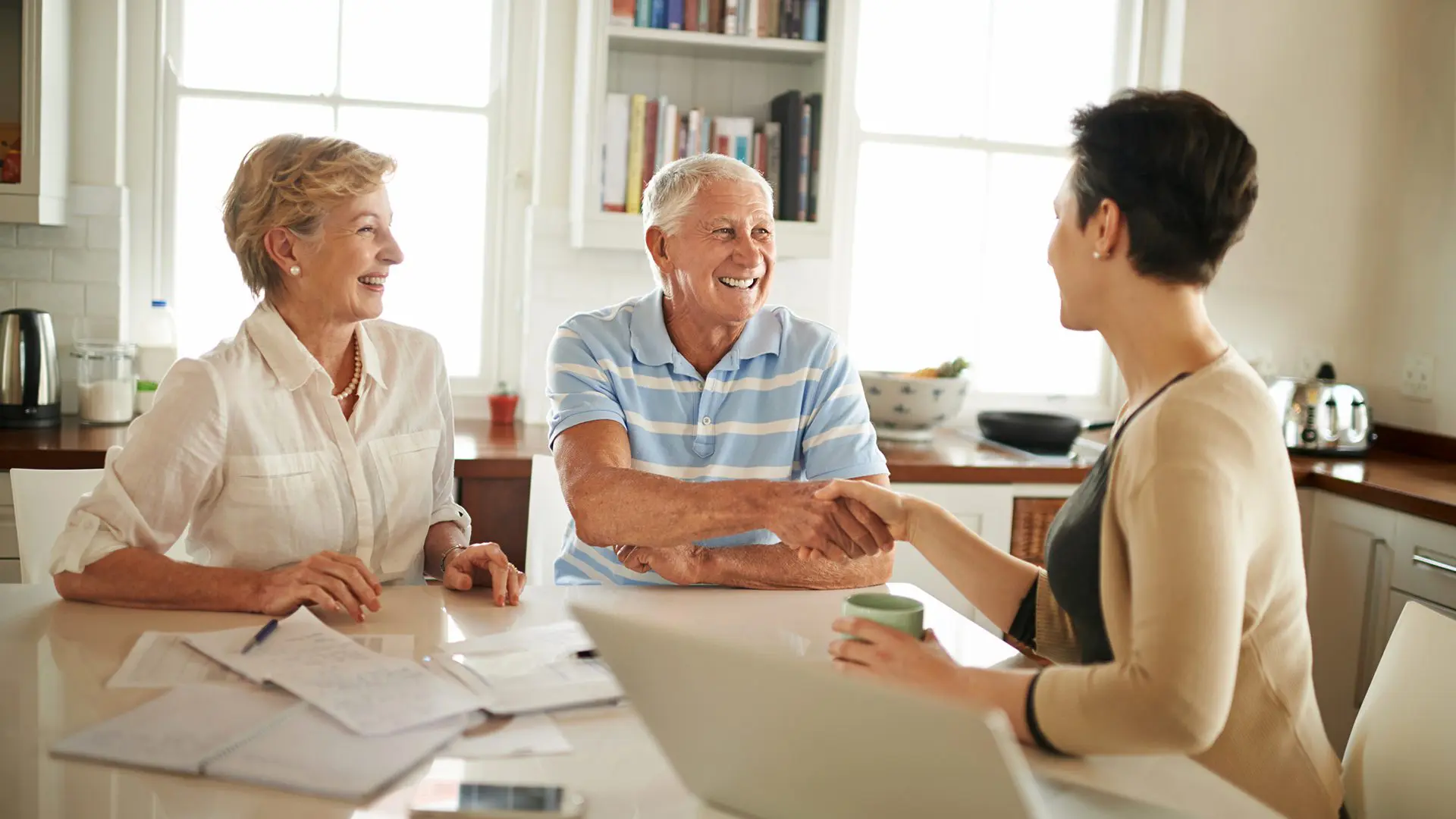 Shot of a senior couple shaking hands with their financial consultant in their kitchen