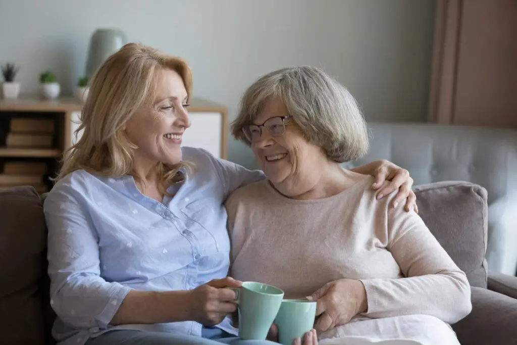 a middle-aged woman sitting on the couch with her arm around her senior mother