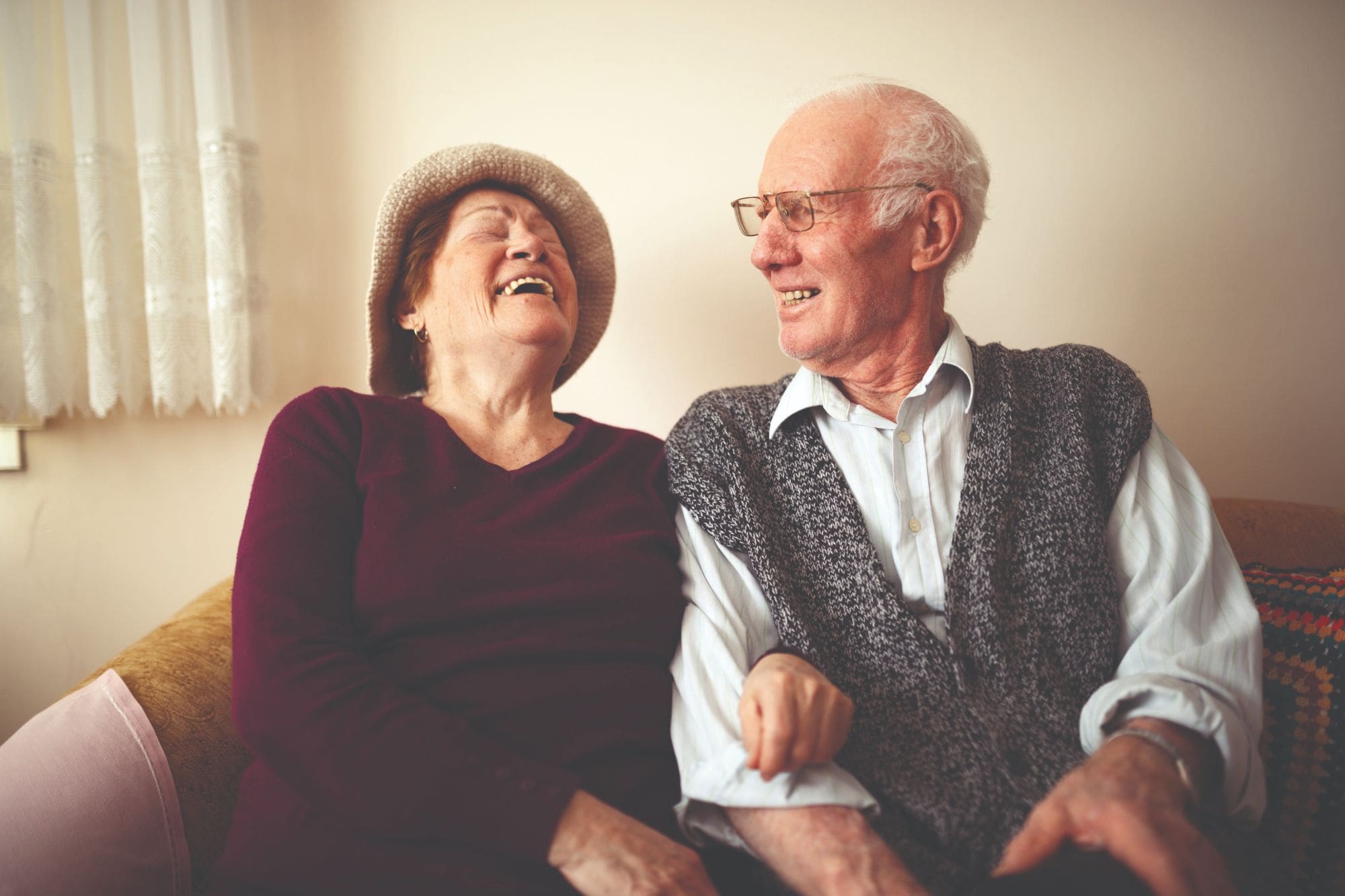Black and white view of older man and woman sitting next to each other on couch and smiling Black and white view of older man and woman sitting next to each other on couch and smiling