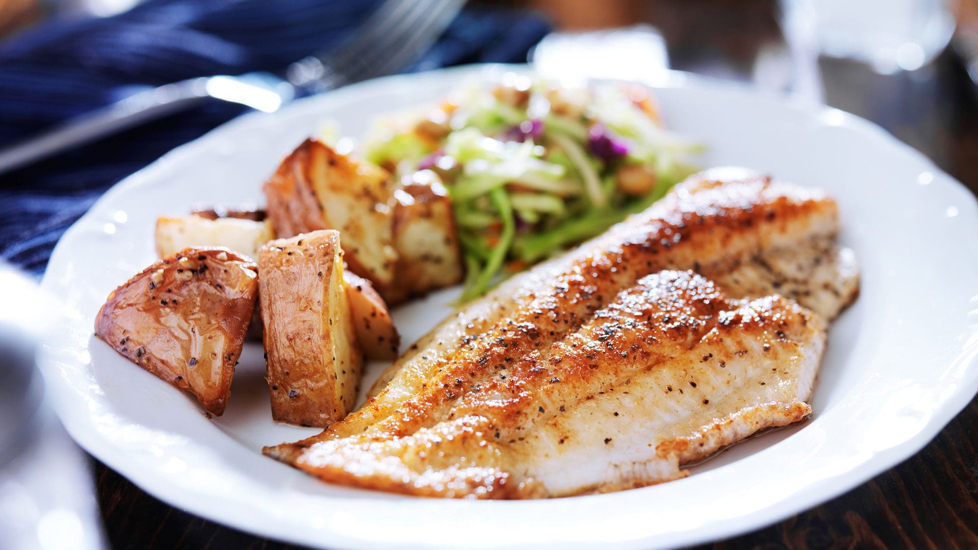 a serving of seared fish, roasted potatoes, and fresh greens on a white dining plate