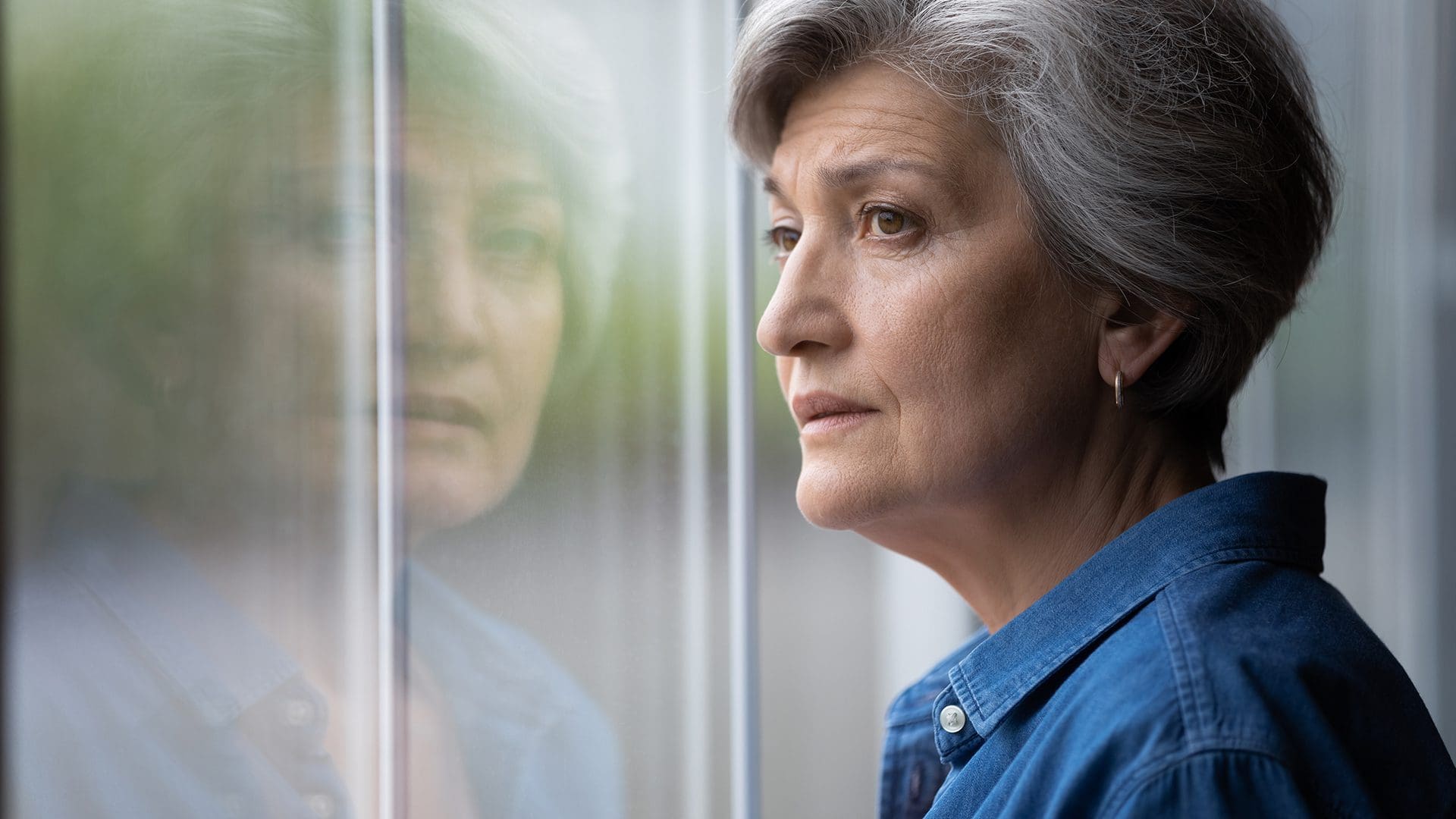 senior woman looking out a window worried