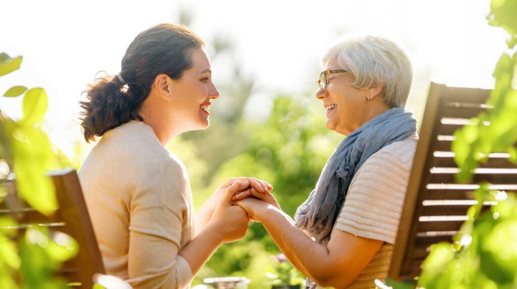 a woman sitting outside and holding the hands of her senior mother